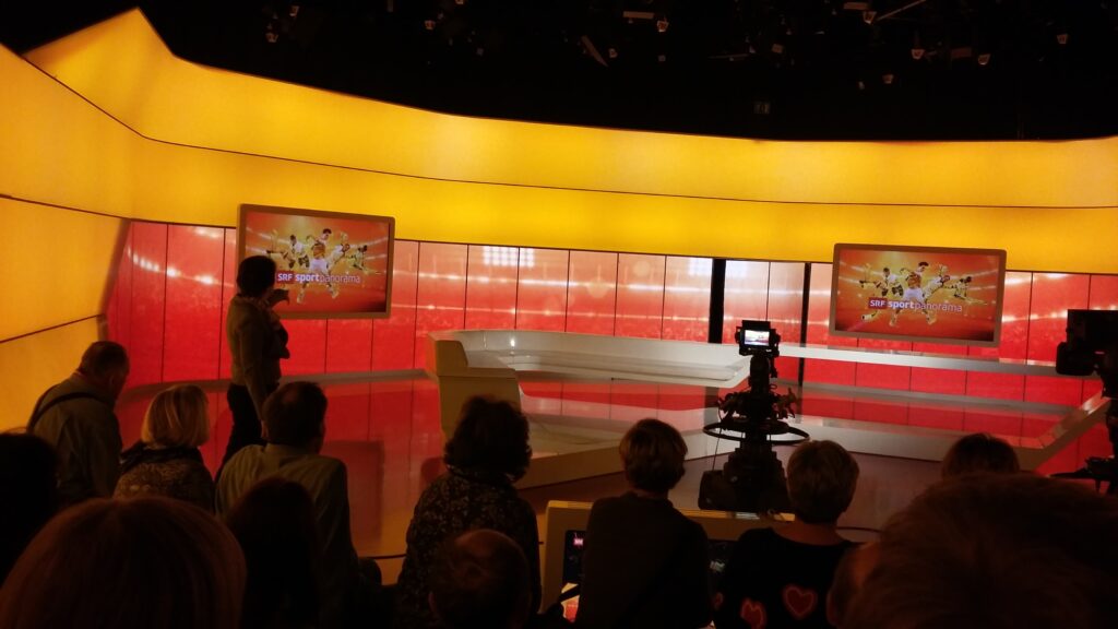 Unsere Führerin erklärt die Funktion der Bildschirme im Sport-Studio.